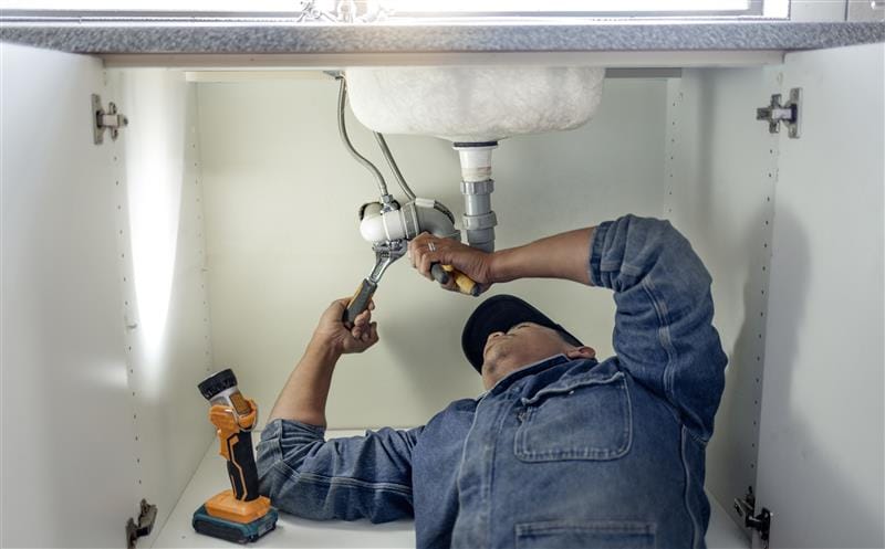 Plumber repairing pipes beneath a bathroom sink in Dana Point